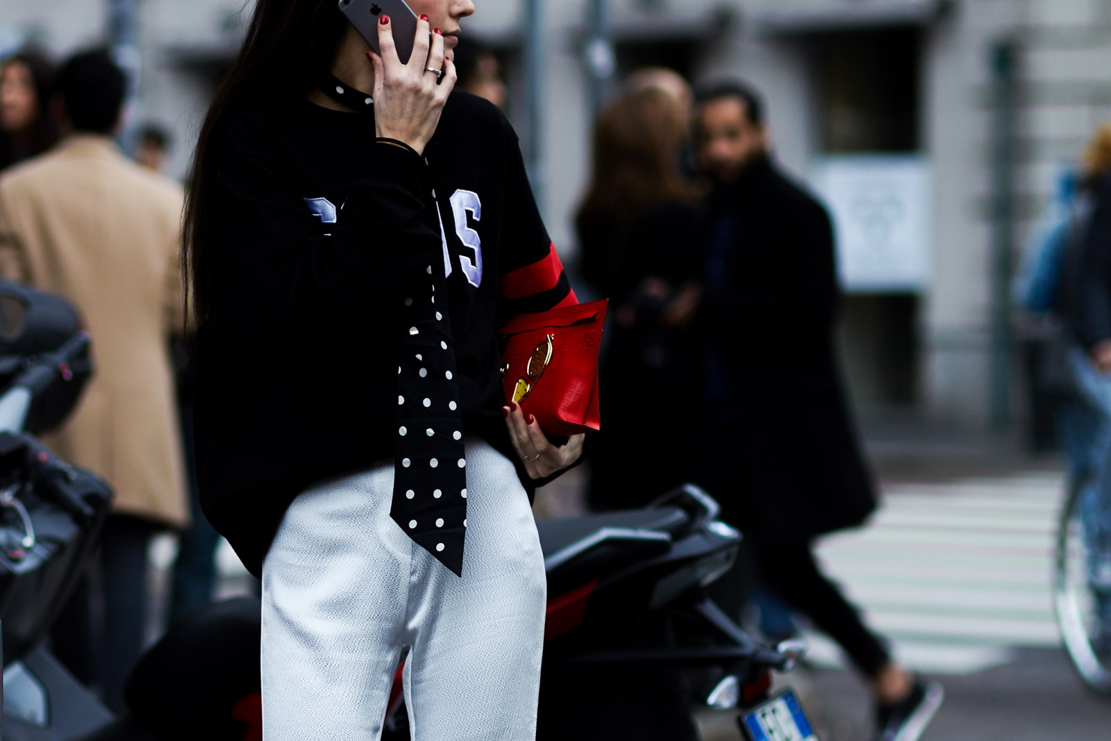 MFW Street Style: Italian stylist Diletta Bonaiuti talking on the phone wearing a black GCDS sweatshirt, polka dot scarf and red Loewe clutch bag in Milan