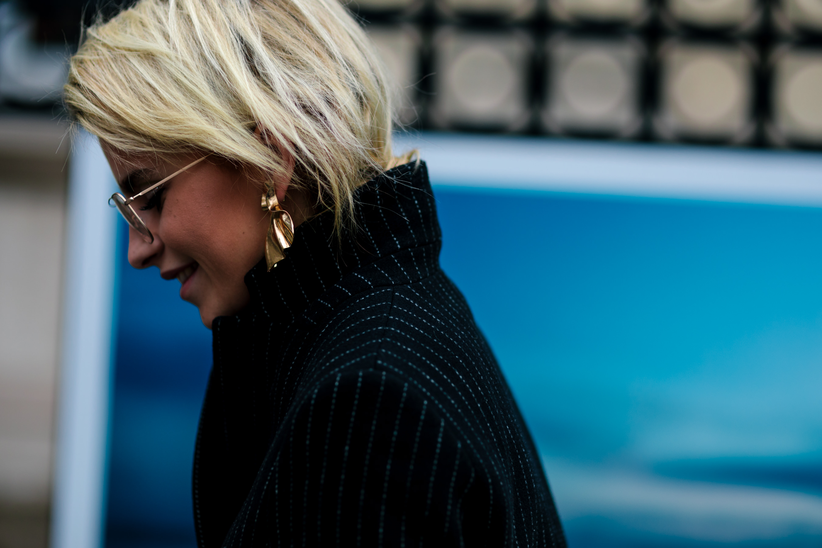 blonde woman wearing gold earrings black coat