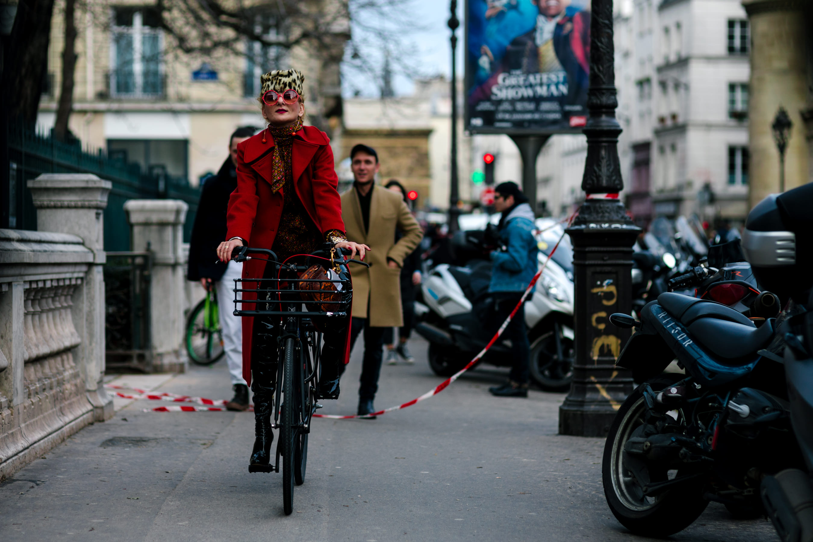 woman wearing red coat leopard hat riding bicycle in Paris